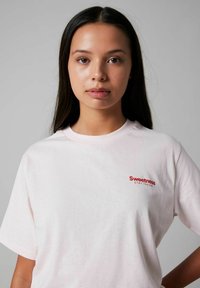 Camiseta de manga corta rosa claro hecha de suave algodón, con un texto bordado en rojo que dice "Sweetness STAY FRESH" en el lado izquierdo del pecho.