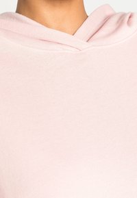 Sweat à capuche rose clair avec une texture douce, doté d'un col rond et d'un design simple, mettant en valeur la surface lisse du tissu.