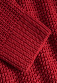 Czerwony dziany materiał z teksturowanym wzorem oraz prążkowanym mankietem. Tkanina ma miękki, ciepły wygląd i równomierne szwy.