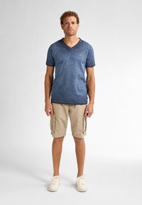 Námořnické tričko s výstřihem do V a texturovanou tkaninou, v kombinaci s béžovými cargo šortkami se bočními kapsami a bílými tenisovými botami na šněrování.