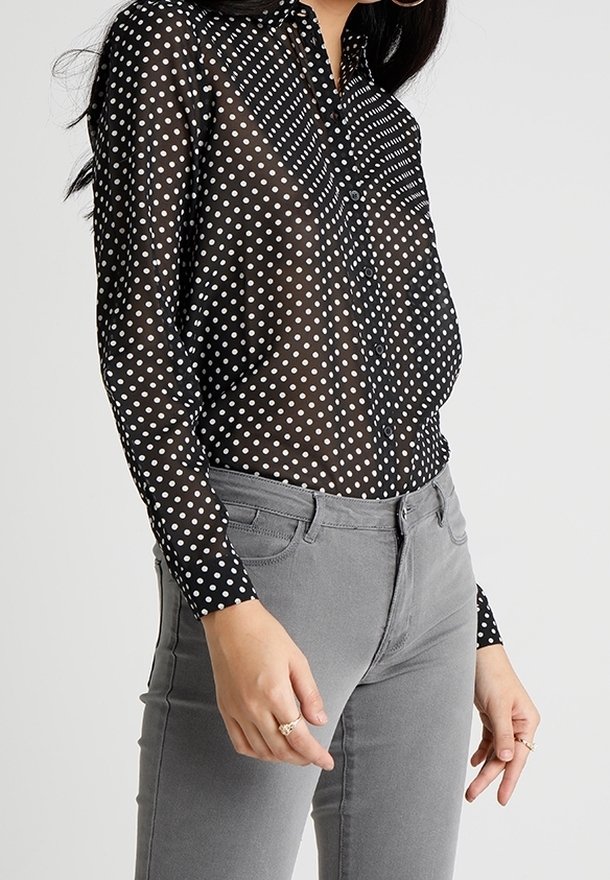Sheer black blouse with white polka dots, button-down front, long sleeves, contrasting striped pattern on shoulders, paired with gray pants.