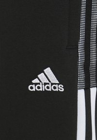 Pantalones deportivos negros de tejido suave, con detalles en tres franjas blancas y el logo bordado de Adidas en la parte frontal.