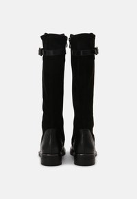 Bottes hauteur genou noires en daim avec une bordure en cuir. Elles présentent une texture lisse, un talon plat et une fermeture éclair à l'arrière.