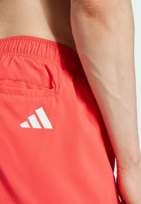 Pantalones cortos deportivos rojos con cintura elástica, bolsillo lateral y un logo blanco en la parte posterior. Tela suave y ligera con un diseño sin costuras.