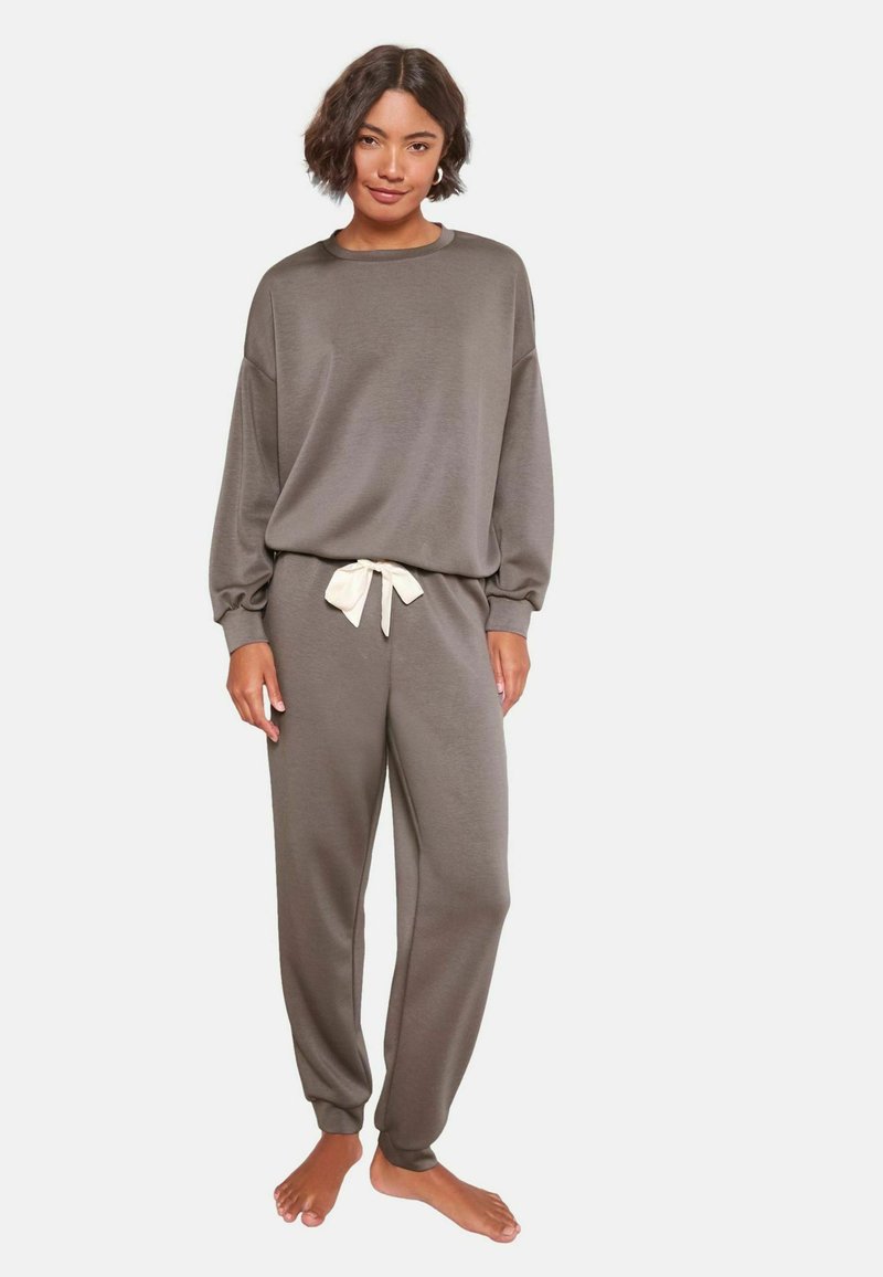 Šedá souprava pohodlného oblečení obsahující svetr volného střihu a zúžené kalhoty s nastavitelnou krémovou šňůrkou v pase. Měkká textilie.