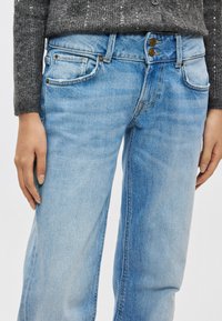 Vaqueros de mezclilla azul claro con cintura alta, que cuentan con dos bolsillos delanteros, botones metálicos y un ligero desgaste. Textura suave y diseño de pierna recta.