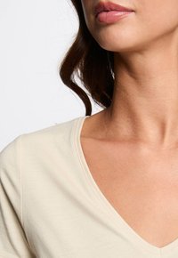 Top de cuello en V en color crema, hecho de suave tela de algodón. Presenta mangas cortas y una sutil textura a lo largo del escote.