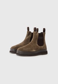 Brown suede ankle boots with elastic side panels, a textured midsole, and pull tabs at the back. Rounded toe and flat rubber sole.