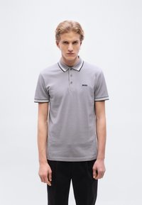 Γκρι πόλο πουκάμισο με μαύρο κεντημένο λογότυπο, με αντιθετικό μαύρο και άσπρο ριγέ γιακά και μανίκια, κατασκευασμένο από απαλό υλικό με μείγμα βαμβακιού.