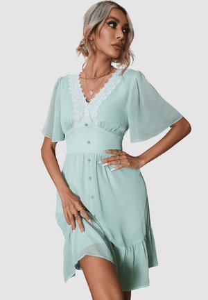 Vestido verde menta claro hecho de tela suave, con un escote de encaje con forma de concha, cortas mangas de volante y detalles de botones en la parte delantera.