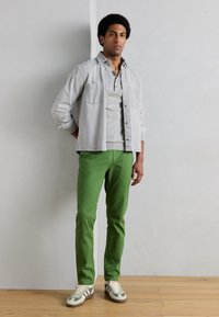 Ανοιχτό γκρι πουκάμισο πάνω από γκρι πόλο, συνδυασμένο με πράσινο παντελόνι και πολύχρωμα αθλητικά παπούτσια. Το πουκάμισο έχει δύο τσέπες στο στήθος και σχέδιο με κουμπιά.