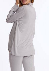 Grijs loungewear-set bestaande uit een langwerpig top met een kraag en een losse pasvorm, gecombineerd met bijpassende broeken. Zachte textuur, minimalistisch ontwerp.