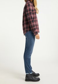 Röd och svart rutig skjorta med långärmar, i kombination med blå denimjeans och svarta snörstövlar med en texturerad sula.