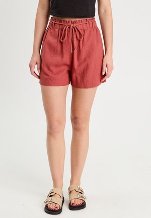 Rust-colored shorts made of lightweight fabric, featuring an elastic waistband with a drawstring. Paired with tan embellished sandals.
