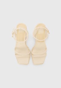 Beige blokkhælte sandaler med fletdetaljer, spænde lukkede ved anklen og firkantet tådesign. Glat tekstur og minimalistisk stil.