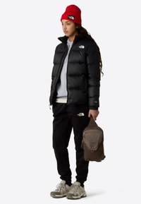 Μαύρο φουσκωτό μπουφάν, γκρι φούτερ με κουκούλα, μαύροι αθλητικοί παντελόνια και γκρι αθλητικά παπούτσια. Κόκκινο πλεκτό σκουφί και καφέ καμβάς σακίδιο με φερμουάρ.