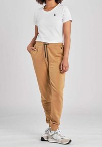 T-shirt bianca con piccolo logo nero, abbinata a joggers beige con vita elastica e coulisse, completata da sneakers grigie.