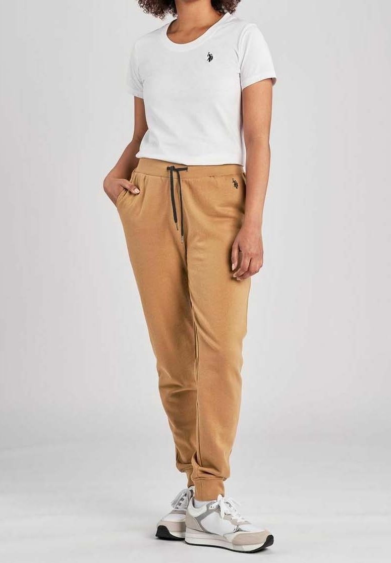 T-shirt bianca con piccolo logo nero, abbinata a joggers beige con vita elastica e coulisse, completata da sneakers grigie.