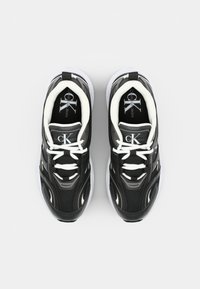 Μαύρα και γκρίζα αθλητικά παπούτσια με διχτυωτό και συνθετικό υλικό, λευκές κορδόνες, πλαϊνές σόλες με επένδυση σε λευκό χρώμα και έντονη επωνυμία στην γλώσσα.