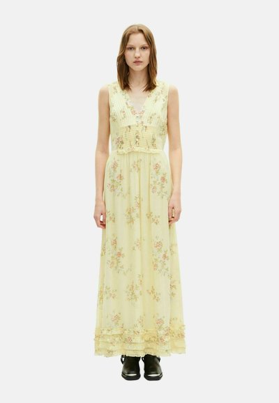 Abito maxi in tessuto giallo chiaro con stampa floreale, scollatura a V, corpetto plissettato e orlo sfrangiato, abbinato a stivali neri alla caviglia.