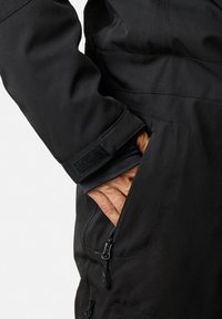 Zwarte waterdichte jas met een zijzak met rits en een manchet met klittenbandsluiting. Soepele textuur en een getailleerde pasvorm.