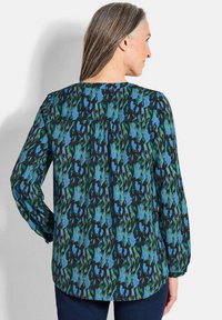 Mehrfarbige Bluse in schwarzem, grünem und blauem abstraktem Muster, mit langen Ärmeln, runder Halslinie und gerafftem Yoke-Detail auf der Rückseite.