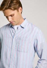 Light blue button-up shirt featuring vertical red stripes, a chest pocket, and a classic collar. Made of a smooth fabric with a relaxed fit.