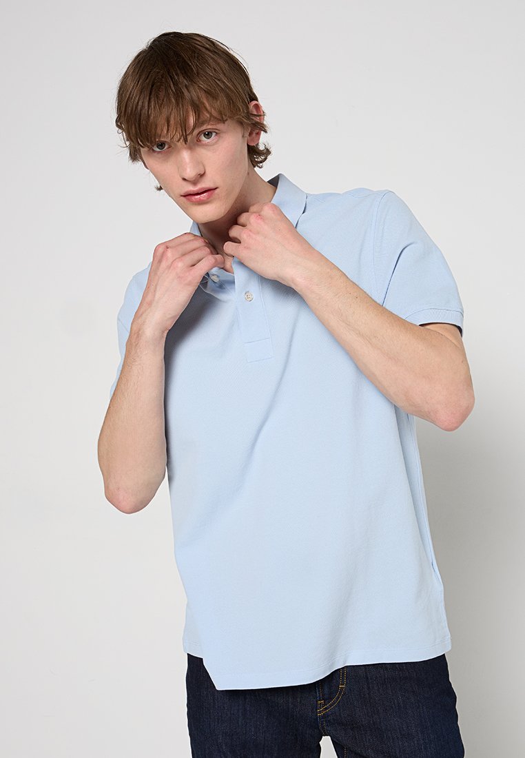 Helles blaues Polohemd aus strukturiertem Stoff, mit klassischem Kragen und kurzen Ärmeln, mit einem einzigen Knopf am Ausschnitt.