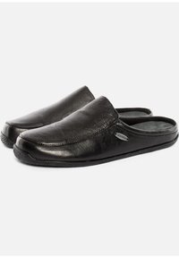 Chaussures glissantes en cuir noir avec une texture lisse, bout arrondi et coutures légèrement surélevées. Présente un logo en accent gris sur le côté.