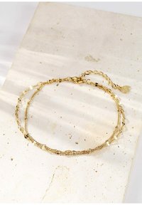 Złota, wielowarstwowa bransoletka z fakturowanymi ogniwami i pewnym zapięciem, z małym urokiem przymocowanym do regulowanego łańcuszka.