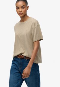 Beige kortærmet t-shirt i blødt stof med en afslappet pasform. Sammen med mørkeblå jeans og et fletbælte i brun.