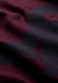 Tessuto a maglia borgogna con un dettaglio decorativo scuro e strutturato. La superficie appare morbida con schemi di filo visibili e una leggera lucentezza.