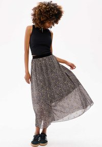 Jupe maxi à imprimé léopard avec une texture légère et fluide, ceinture noire, et un haut sans manches noir ajusté. Des baskets noires complètent le look.