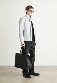 Gaišpelēka lādēta pūkains mētelis ar augstu apkakli, melns tops, melnas džinses un teksturēta melna somiņa ar "HUGO" logotipu. Melnas kurpes.