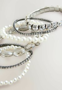 Collection of bracelets featuring pearls, clear crystals, and metal accents in silver and black, showcasing varied textures and designs.