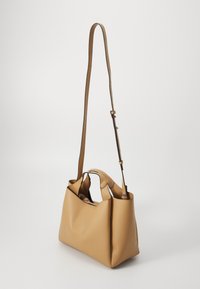 Sac à main en cuir tan avec une finition texturée, deux poignées supérieures et une longue sangle réglable. Design à ouverture supérieure avec un intérieur visible.