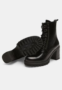 Botine negre din piele, cu toc gros, vârful rotund, șireturi în față și fermoar lateral. Au un talpă texturată pentru aderență.