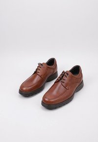 Brown leather shoes with a textured finish, lacing detail, and rubber soles, featuring a sleek design and contrasting stitching accents.