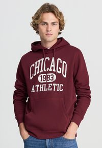 Felpa maroon con tasca frontale, con il testo "CHICAGO 1983 ATHLETIC" in bianco. Tessuto morbido, cappuccio con coulisse e polsini a costine.