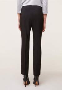 Svarta skräddarsydda byxor med en slät yta, med en midjehöjd i normal höjd och raka ben, tillsammans med svarta högklackade skor.