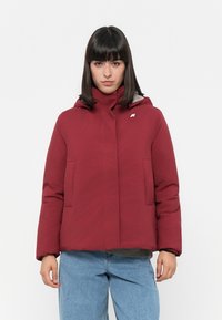 Rote gepolsterte Jacke mit Kapuze, mit grauem Innenfutter, zwei Fronttaschen und einem kleinen Logo auf der Brust.