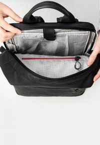 Borsa nera con finitura texturizzata, dotata di un ampio interno, foderata con motivo a griglia grigia, tasca con zip rossa e doppi manici.