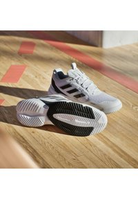 Białe buty sportowe z czarnymi akcentami, teksturowana cholewka i wzorzysta podeszwa. Zawierają wyraźny wzór z trzema paskami i wyściełany kołnierz.