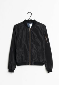 Czarna kurtka bomberka wykonana z gładkiego, lekkiego materiału. Ma zamek z przodu, ściągacze przy mankietach oraz zasuwaną kieszeń na rękawie. Wisi na haku.