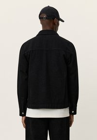 Μαύρο μπουφάν από τζιν με λουλουδάτο μοτίβο, μανσέτες με κουμπιά, γιακά και ευθεία τελείωμα. Φορεμένο πάνω από ένα λευκό μπλουζάκι και συμπληρώνεται με καπέλο.