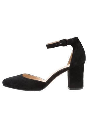 Black suede high-heel shoe with a pointed toe, ankle strap, and block heel. The interior features a light lining. Minimalist design.