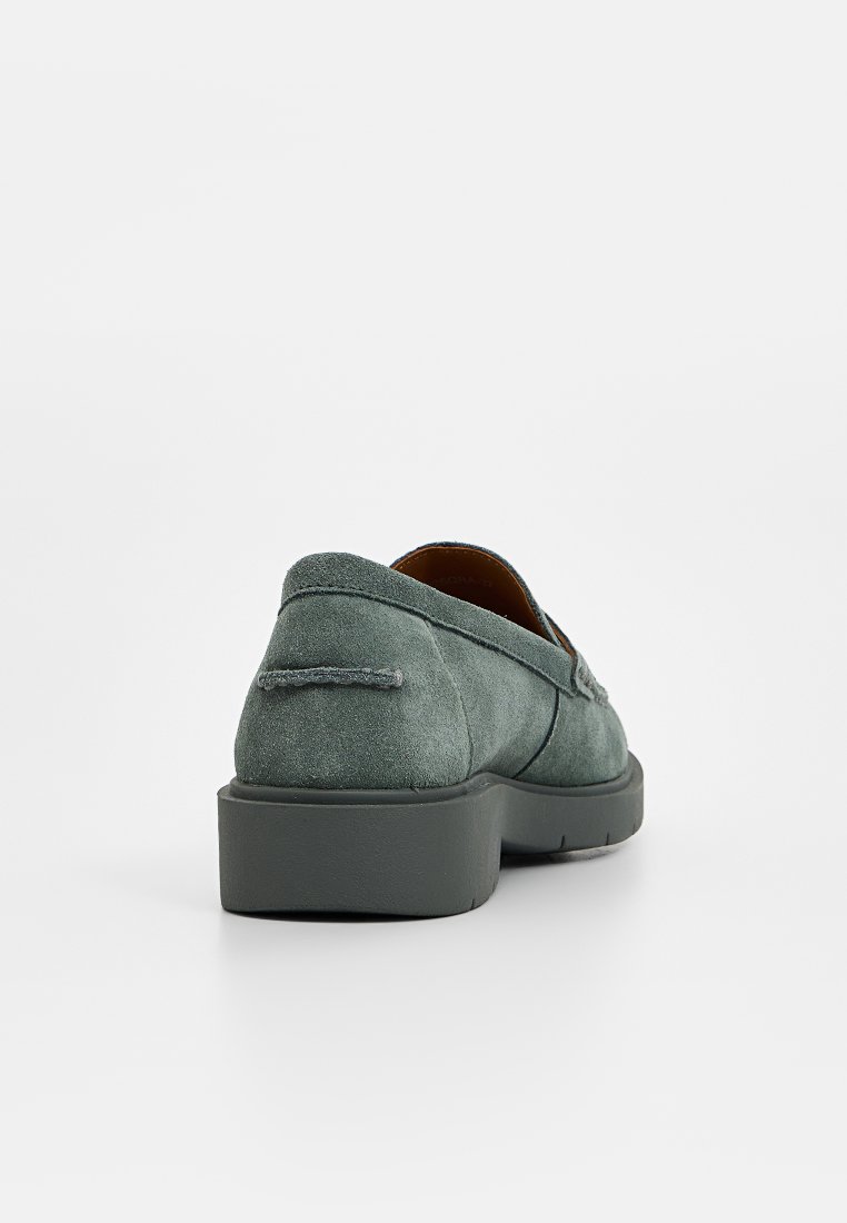 Des chaussures en suède vertes à enfiler, avec un bout arrondi, une semelle à plateforme basse et un détail de broderie décoratif au niveau du talon.