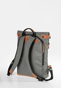 Grau rucksack mit braunen Lederakzenten, verstellbaren schwarzen Trägern, rutschfester Oberseite und äußeren Reißverschlusstasche. Robuste Materialoberfläche.