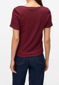 Burgunderfarbener gerippter Kurzarm-Top mit rundem Ausschnitt, kombiniert mit dunkelblauen Denim, die über klassische Nähte und ein figurbetontes Design verfügen.