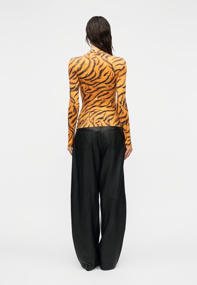 Μπλούζα με μακριά μανίκια σε πορτοκαλί και μαύρο μοτίβο ριγέ τίγρης, συνδυασμένη με φαρδιά μαύρα δερμάτινα παντελόνια. Ομαλή υφή και εφαρμοστή σχεδίαση.